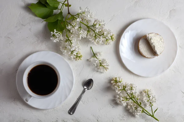 A cup of coffee, cakes and lilac flowers are on the table. On a white background.