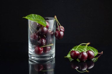 Masada bir bardakta kiraz var. Siyah bir arka planda. Alçak tuş.