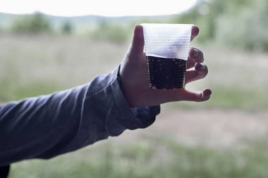 Ormanda, bir kız elinde plastik bir bardak tutuyor. Yarısı içki dolu..