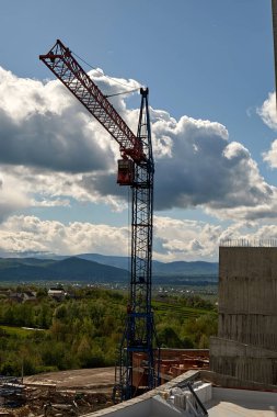 Dağlardaki bir inşaat alanında vinç kaldırma. Mavi gökyüzünün arka planında bulutlar.