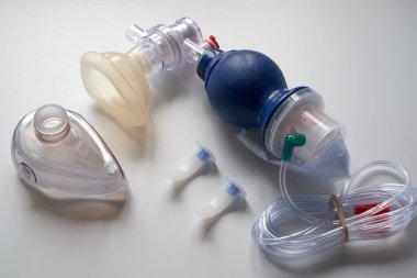 Masanın üzerinde oksijen maskesi ve tıbbi hava yolu olan bir Ambu çantası var. Beyaz bir arka planda..