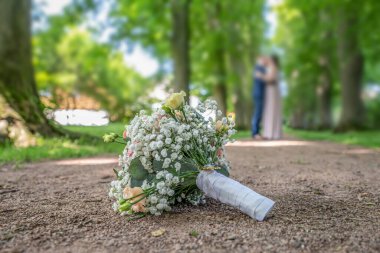 Bulanık bir çiftin ön planında düğün buketi. Çiçekler ve aşıklar.