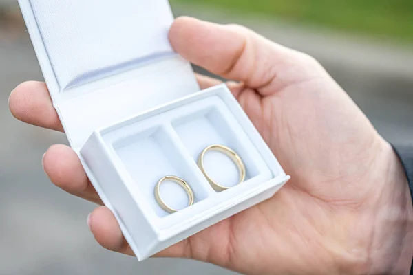 新郎手牵着浪漫的婚姻新人的结婚戒指装在一个白色的盒子里 — 图库照片