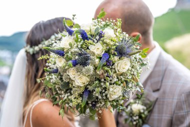 Bulanık bir çiftin ön planında düğün buketi. Çiçekler ve aşıklar.