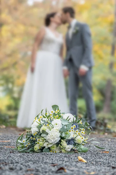 Wedding bouquet on foreground of a blurred kissing couple. Flowers and lovers.