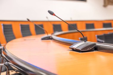 Mikrofonlar ve boş bir konferans odasında yuvarlak kahverengi masa. Siyah sandalyeyle toplantı başlıyor..