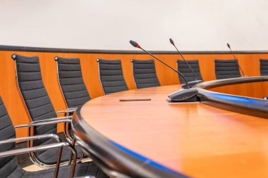 Mikrofonlar ve boş bir konferans odasında yuvarlak kahverengi masa. Siyah sandalyeyle toplantı başlıyor..