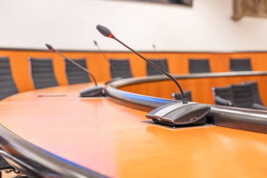 Mikrofonlar ve boş bir konferans odasında yuvarlak kahverengi masa. Siyah sandalyeyle toplantı başlıyor..