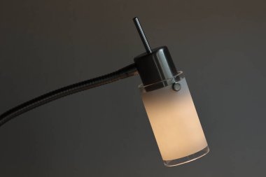 Buzlu cam ve metal standı olan modern masa lambası. Ilık yumuşak ışık rahat ve minimalist bir atmosfer yaratır..