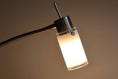 Buzlu cam ve metal standı olan modern masa lambası. Ilık yumuşak ışık rahat ve minimalist bir atmosfer yaratır..