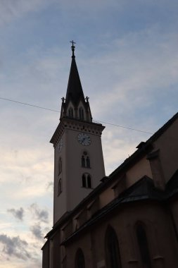 Gotik bir kule ve üzerinde bir saat var ve akşam gökyüzü ile çapraz. Yumuşak doğal ışıkta eski bir kilisenin mimari ayrıntıları.