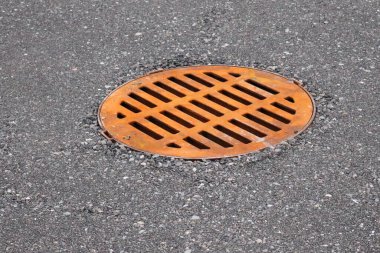 Taze asfaltta turuncu metal yağmur gideri kapağı. Kentsel altyapı minimal ve grafik tarzda kaydedildi.