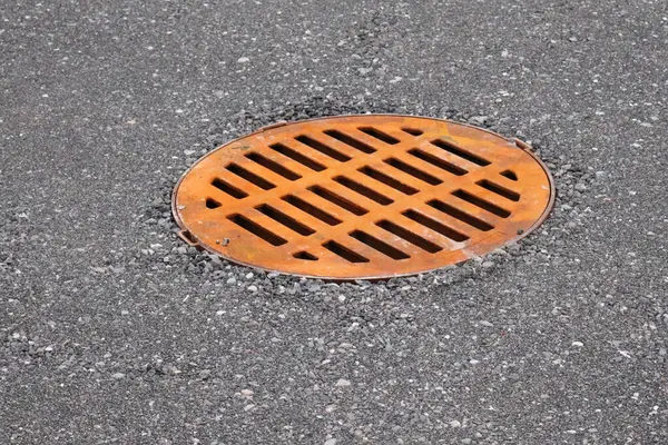 Taze asfaltta turuncu metal yağmur gideri kapağı. Kentsel altyapı minimal ve grafik tarzda kaydedildi.