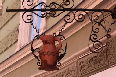 Tarihi bir binanın ön cephesinde dekoratif paslı bir sürahinin asılı olduğu eski dövmeli bir demir levha. Muhtemelen eski bir meyhaneden ya da dükkandan gelen tabela sokağa karakter ve cazibe katıyor.. 