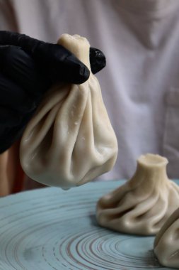 Geleneksel Gürcü hamur tatlısı khinkali tabağın üzerinde siyah bir eldiven ile tutuldu. Hamur köftesinin içinde kıvrık ve sulu bir dolgu var..