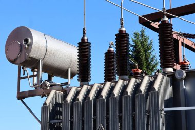 Soğutucu yüzgeçleri, yüksek voltajlı yalıtıcıları ve kablosu olan bir güç dönüştürücünün yakın çekimi. Mavi gökyüzü altında endüstriyel elektrik altyapısı.