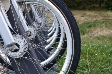 Bisiklet paylaşım istasyonunda sıraya dizilmiş bisiklet tekerleklerinin yakın görüntüsü. Odaklı konuşmalar ve lastikler, arka planda yeşil çimenler.