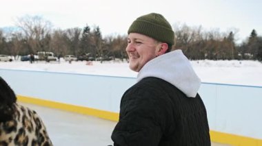 Sıcak kış kıyafetleri içinde kız ve erkek buz pateni yapıyor. El ele tutuşup gülüyorlar. Açık havada parkta eğleniyorlar. Mutluluk ve eğlence kavramı. Yüksek kalite 4k görüntü