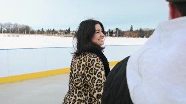 Sıcak kış kıyafetleri içinde kız ve erkek buz pateni yapıyor. El ele tutuşup gülüyorlar. Açık havada parkta eğleniyorlar. Mutluluk ve eğlence kavramı. Yüksek kalite 4k görüntü