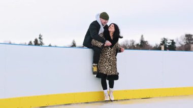 Buz pateni pistinin dışında şık giyinmiş mutlu, genç bir çift. Noel gecesi öpüşen ve kucaklaşan romantik partnerler. Aydınlanmış şehirde kış tatili mevsimi. Yüksek kalite 4k görüntü