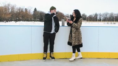 Termostan çay içen ve kış tatillerinde buz pateni pistinde romantik bir buluşma sırasında sohbet eden beyaz bir çift. Yüksek kalite 4k görüntü