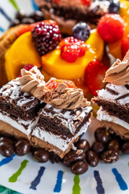 Çilek, yaban mersini ve mango dilimleri gibi taze meyvelerle çevrili çırpılmış krema ve çikolata parçalarıyla kaplı renkli bir tatlı tabağı ve kahve çekirdekleri..