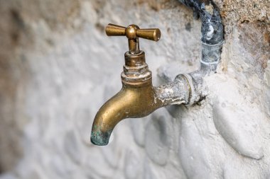 Eski bir pirinç musluğun yakın plan çekimi taş bir duvara bağlanmış, aşınma izleri ve aşınma izleri var..
