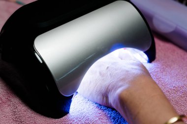 Bir güzellik salonunda UV lambasının altında yeni boyanmış tırnaklarını kurutan bir kadın.