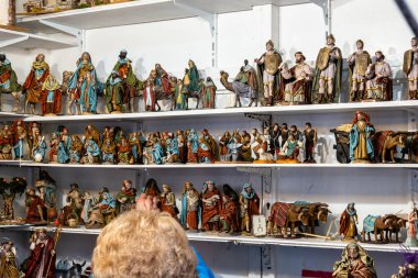Bir el dolusu renkli Noel doğumu figürleriyle dolu rafları gösteren yaşlı bir kadın.