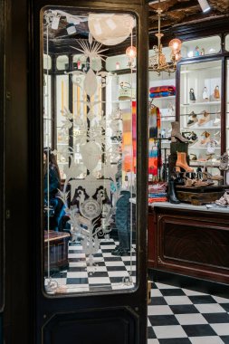 Barselona, İspanya-5 Ocak 2025. Süslü cam bir kapıdan şık bir ayakkabı mağazasına bakın, rafları ayakkabılarla, renkli eşarplarla, ve kareli bir zemin