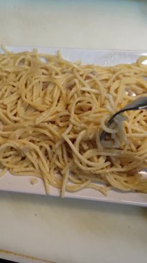 Kremalı spagetti carbonara beyaz bir tabaktan çatalla kaldırılıyor.
