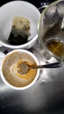 Çay poşeti ve metal lavaboda kaşıkla kirli bardaklarda kalan kahve ve çay.