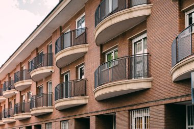 Balkonları ve metal parmaklıkları olan kırmızı tuğlalı apartman, modern şehir konutlarını ve mimariyi temsil ediyor.
