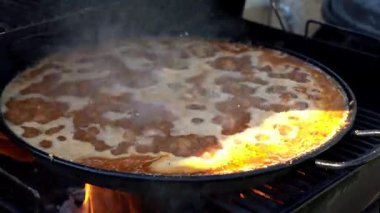 Büyük tavada geleneksel İspanyol paella ızgarada odun ateşinde pişiyor buhar ve lezzetli aromalar yaratıyor.