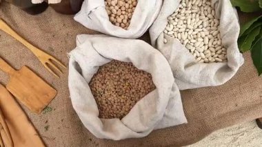 Nohut, beyaz fasulye ve bez çuvalların içindeki mercimek çuval kumaş, ahşap kap kacak ve otlarla çevrili..