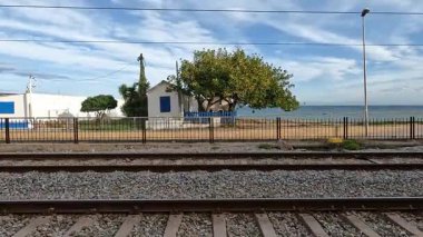 Yakınlarda küçük beyaz ve mavi bir ev bulunan pitoresk bir sahil şeridi boyunca uzanan raylar.