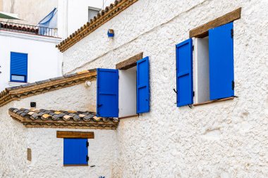 Beyaz sıva duvarlı, tahta aksanlı ve açık pencereli geleneksel Akdeniz evi. Bir kıyı köyünde kırsal Avrupa mimarisi.