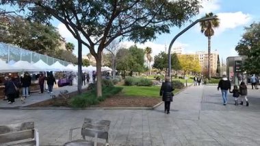 Badalona, İspanya-31 Mart 2025. İspanya 'nın Badalona kentindeki Plaza Pompeu Fabra' da canlı bir açık hava pazarı, beyaz çadırların, satıcıların, alışverişçilerin ve yeşil bir şehir parkının yer aldığı.