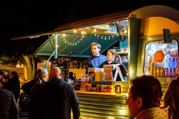 Barselona, İspanya-25 Kasım 2023. Mobil fast food servisi için modifiye edilmiş bir kamyonun önünde yemek yerken eğlenen bir grup insan. Yemek kamyonu