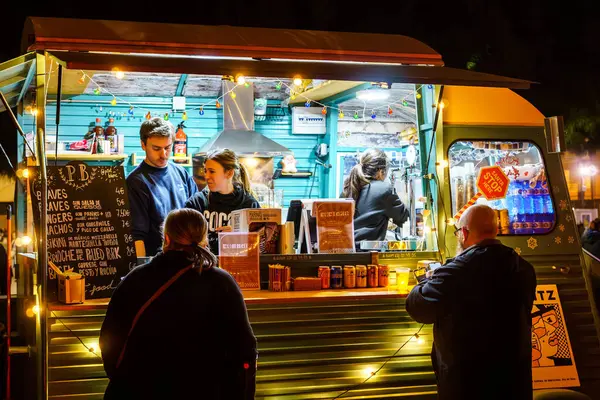 Barselona, İspanya-25 Kasım 2023. Mobil fast food servisi için modifiye edilmiş bir kamyonun önünde yemek yerken eğlenen bir grup insan. Yemek kamyonu