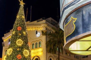 Aydınlatılmış Noel ağacı ve süslemesi olan şenlikli bir mimari. Badalona, İspanya