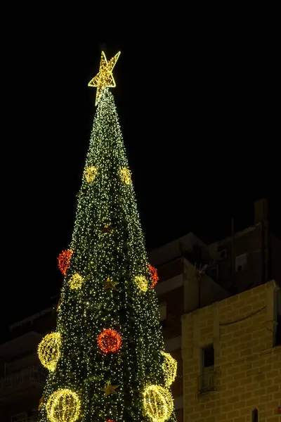Aydınlatılmış Noel ağacı ve süslemesi olan şenlikli bir mimari. Badalona, İspanya