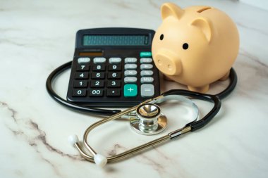 Hesap makinesi ve steteskobu olan bir kumbara sağlık hizmetlerinin finansal yönünü gösteriyor..