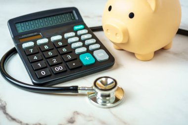 Hesap makinesi ve steteskobu olan bir kumbara sağlık hizmetlerinin finansal yönünü gösteriyor..