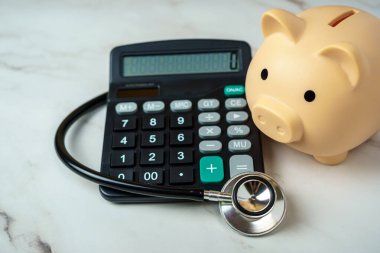 Hesap makinesi ve steteskobu olan bir kumbara sağlık hizmetlerinin finansal yönünü gösteriyor..