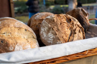 Masanın üzerinde bir sepet ekmek oturuyor. Ekmek farklı şekil ve boyutlarda ve bazılarının kabuğu var. Sepet beyaz bir kumaşın üzerine konur. Sahneye biraz zarafet katar.