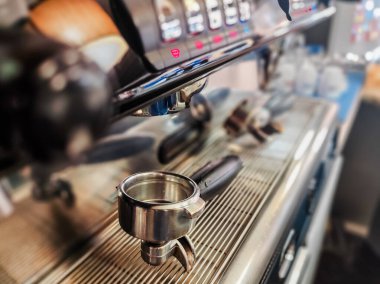 Espresso demlemek için hazır bir portatif filtresi olan bir kahve makinesinin yakın çekimi. Parlak metal yüzey makinenin kontrol ve çevresini yansıtıyor, kahve yapma sürecini vurguluyor..