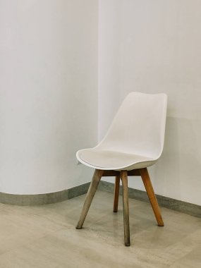 Minimalist, tahta bacaklı, düz bir duvara yaslanmış beyaz bir sandalye..