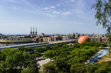 Badalona, İspanya-23 Haziran 2024. İspanya 'nın Badalona kentindeki enerji kulelerinin doğal bir parktan panoramik görüntüsü. Doğa ve endüstri arasındaki uyum, ikonik üç bacaya bakan bir parktan elde edildi..