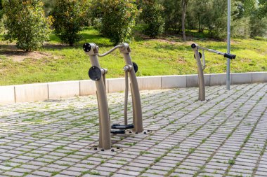 Bir park ortamında asfalt bir alanda açık hava fitness ekipmanları.